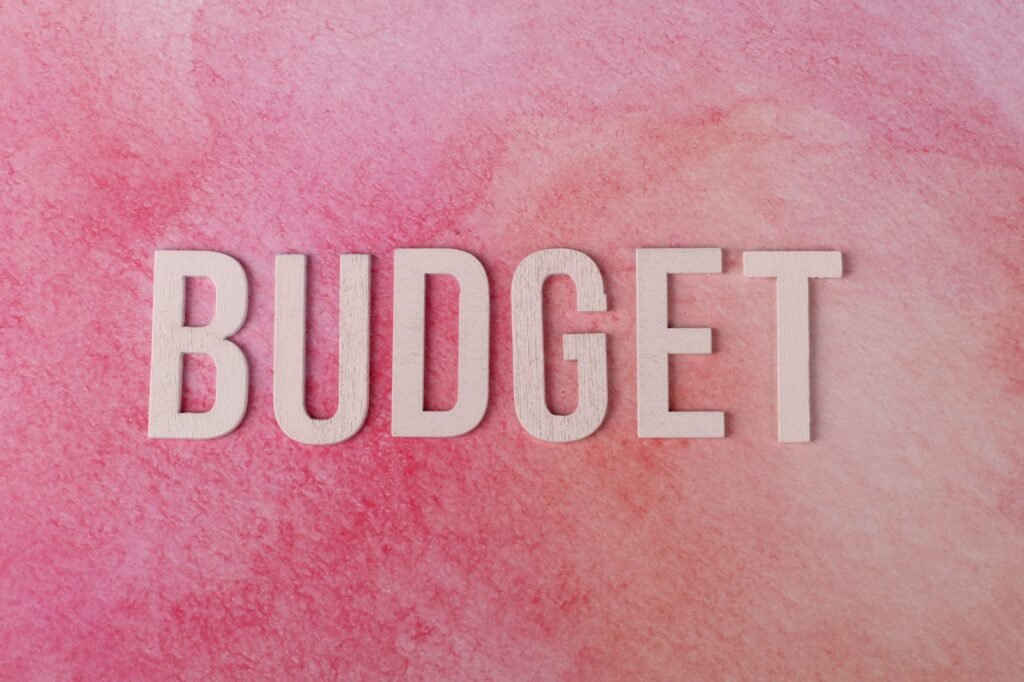 The word 'BUDGET' on a pink textured background emphasizes financial planning.