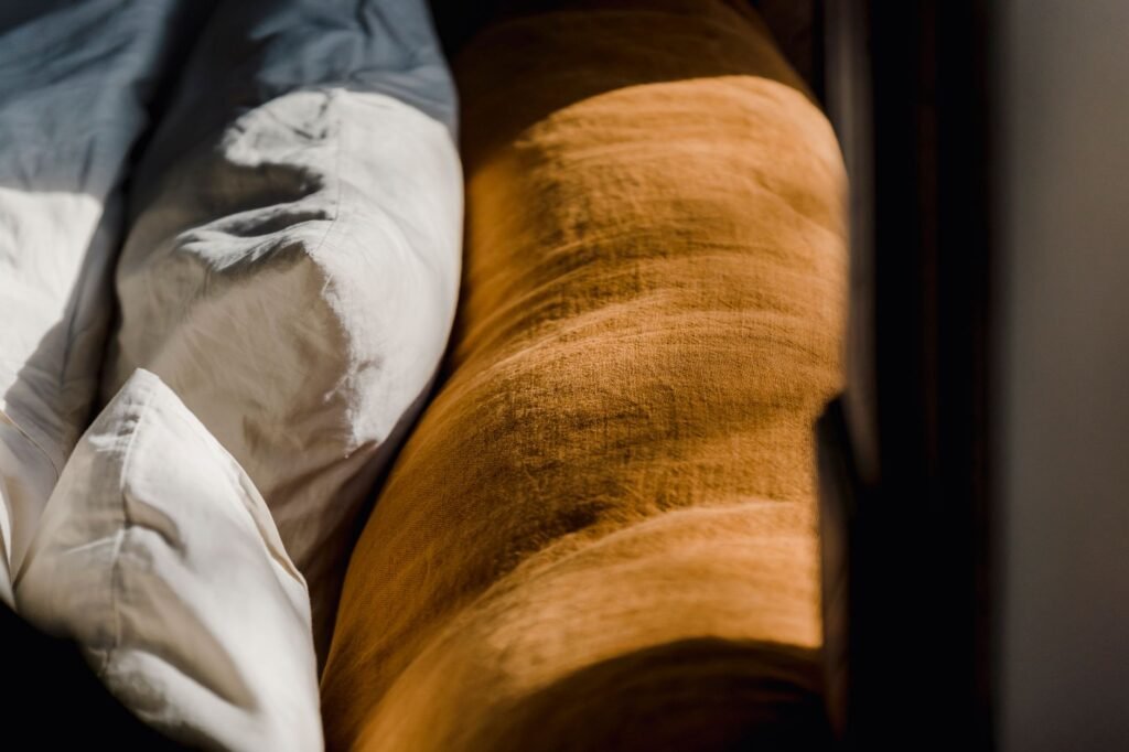 Soft cozy back of brown couch and cushions in white cotton sheets under sunshine from window
