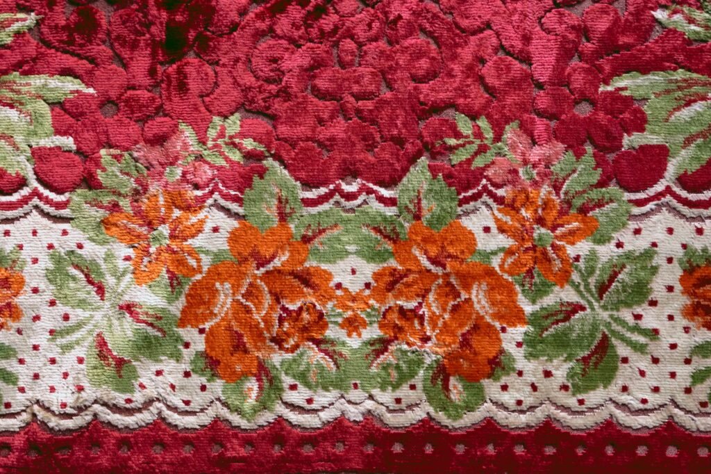 Colorful floral textile design with red, orange, and green in a rich, textured pattern.